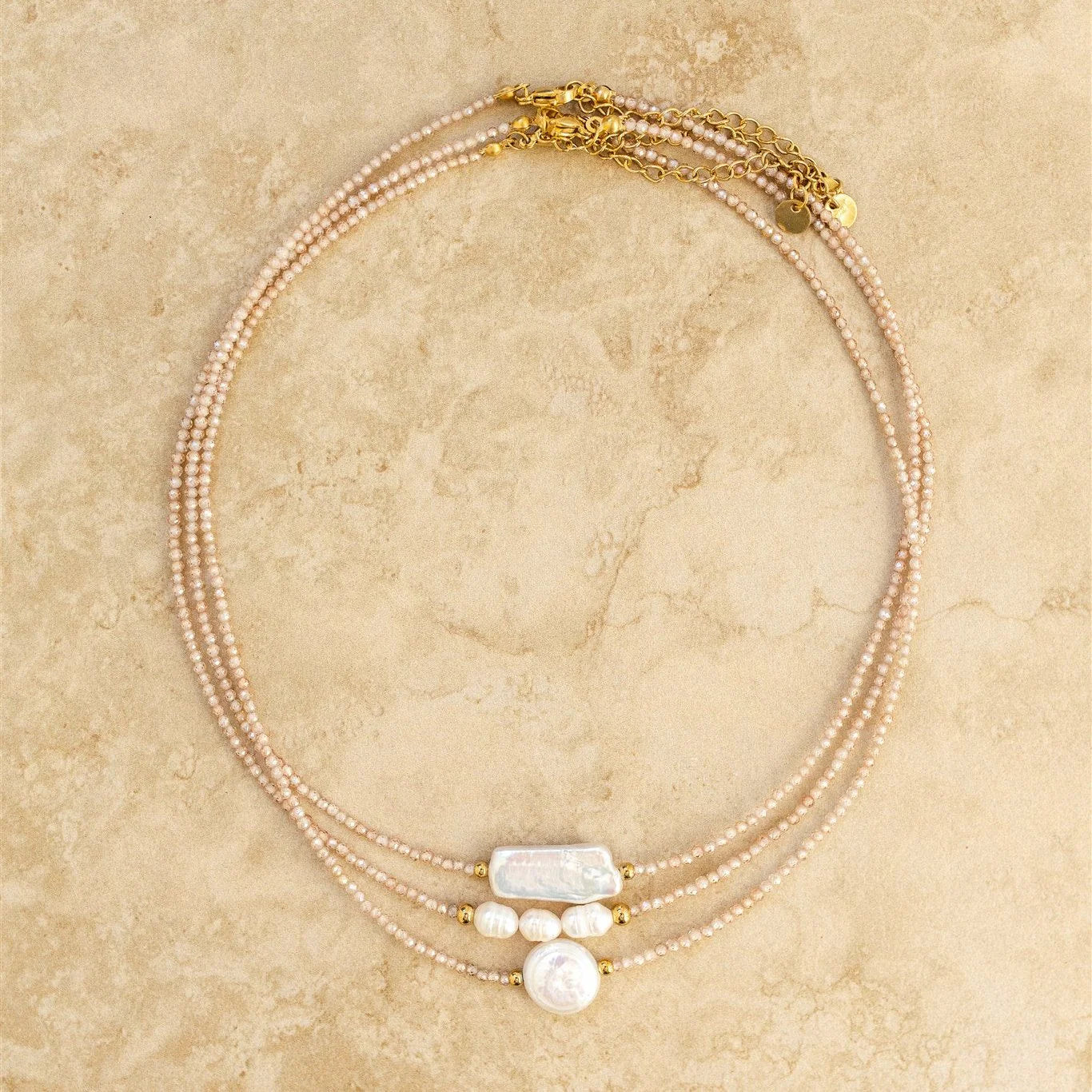 Multi-strand pearl necklace with gold accents on a beige marble surface
