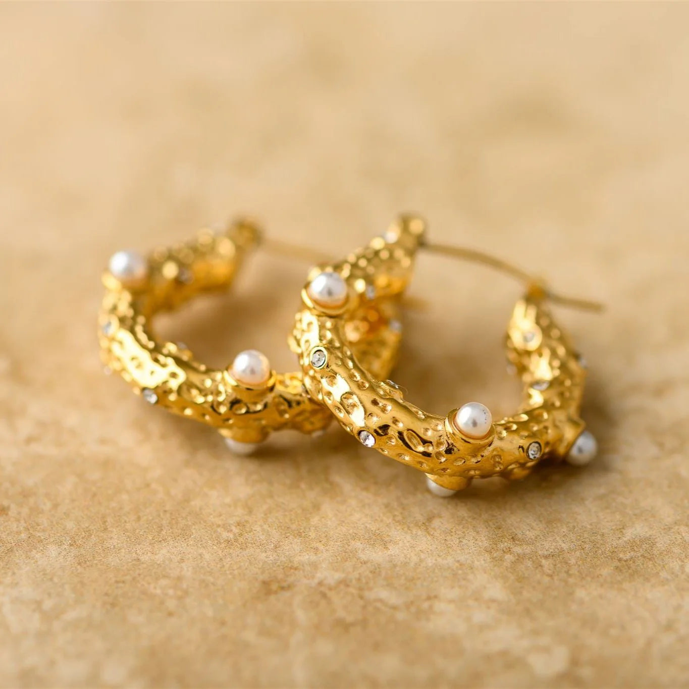 Gold hoop earrings with pearl accents on a beige background