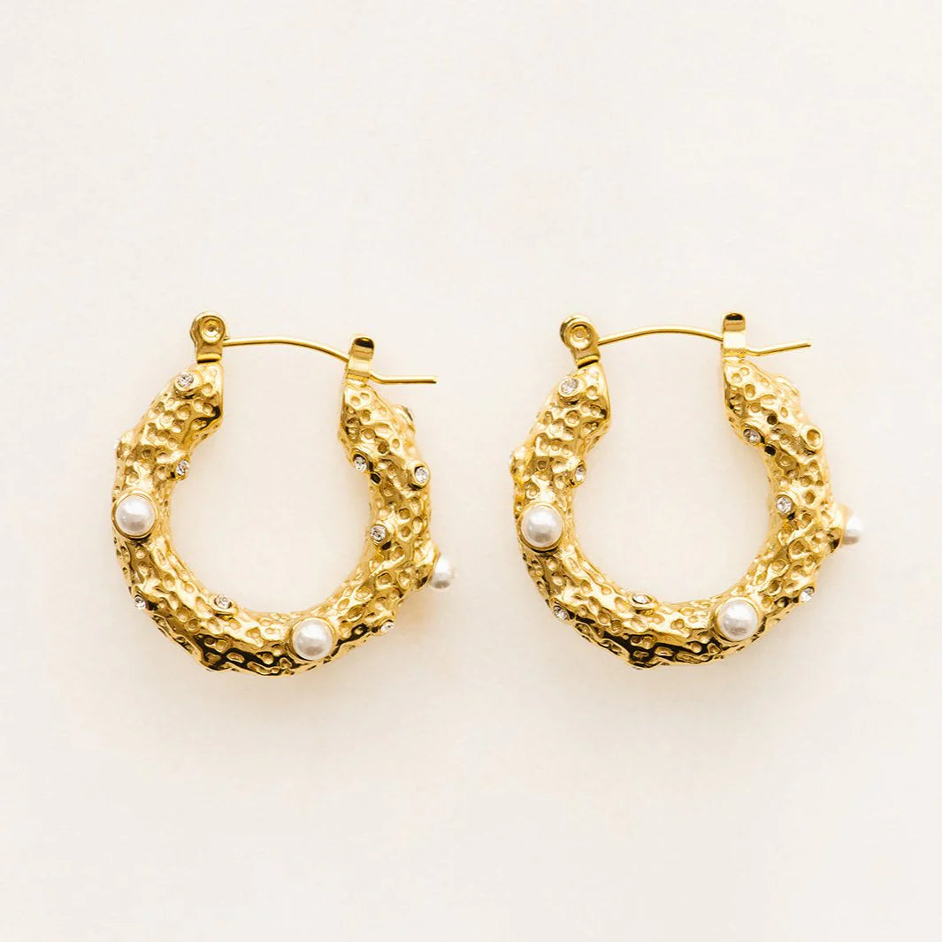 Gold hoop earrings with pearl accents on a light beige background