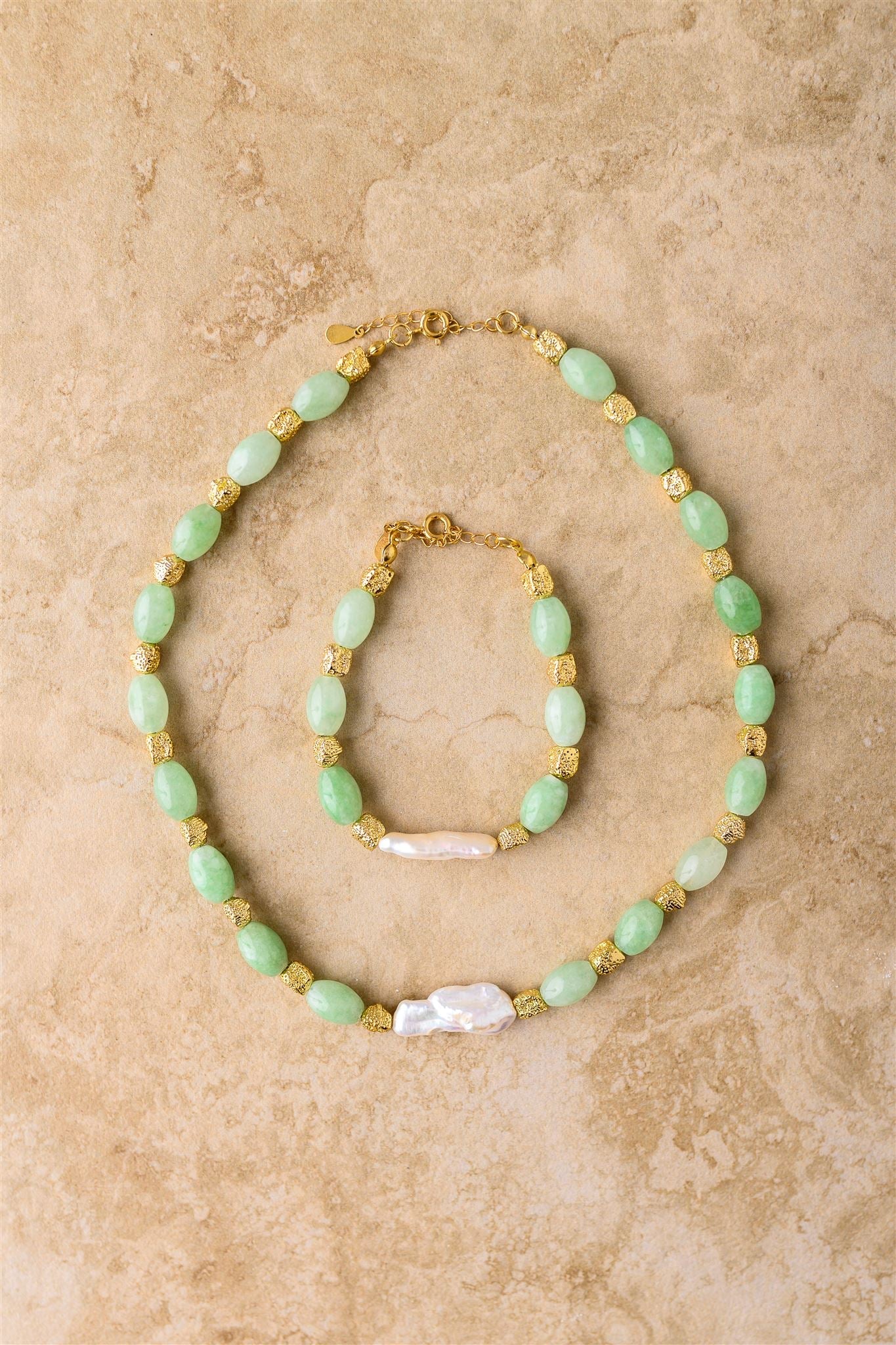 Necklace with green beads and gold accents on a beige stone surface