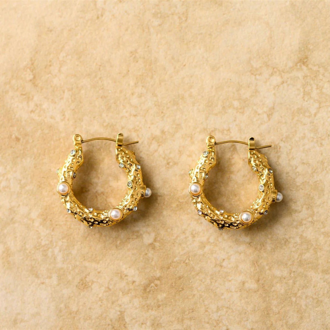 Gold hoop earrings with pearl accents on a beige background