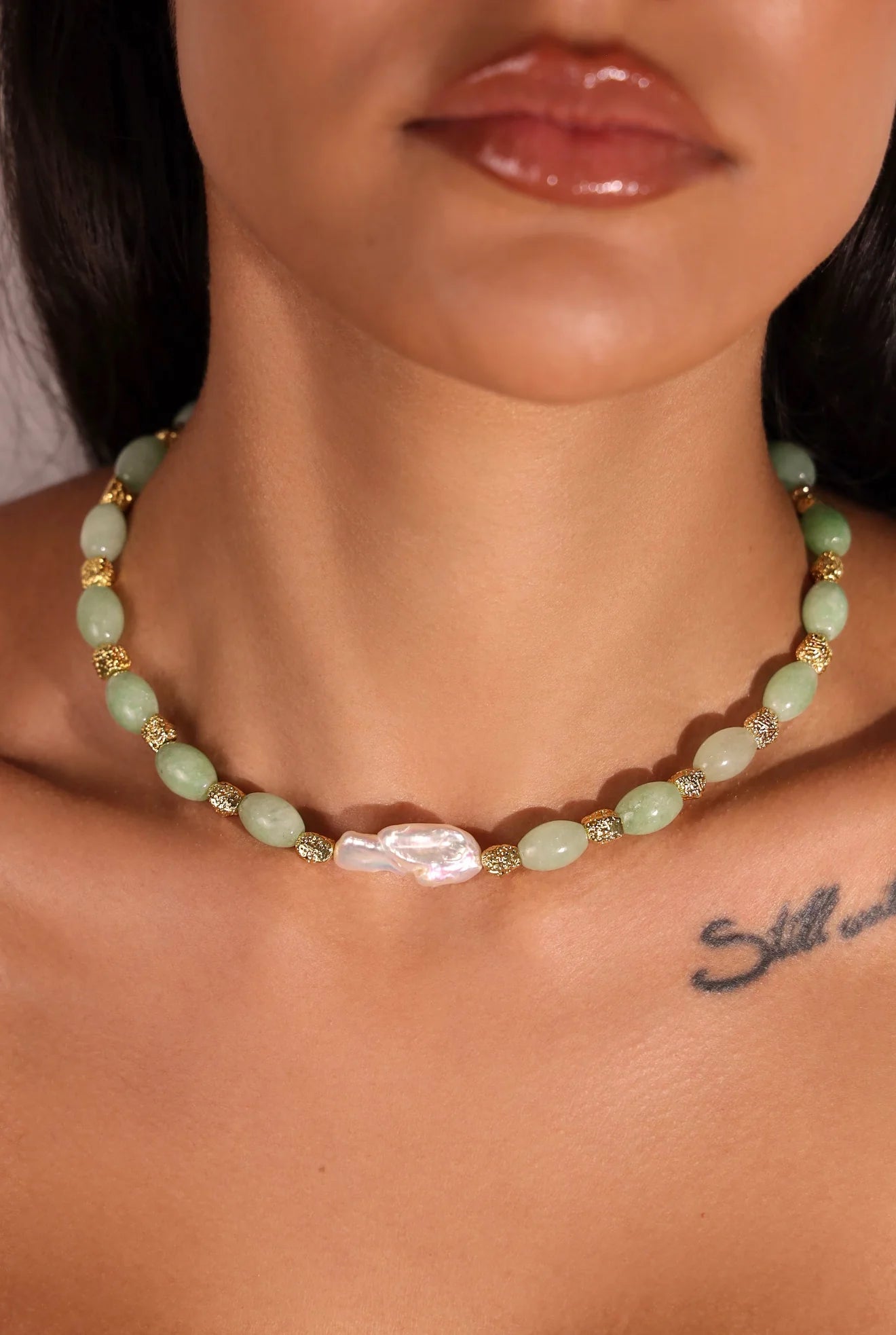 Close-up of a person wearing a green beaded necklace with a central pearl