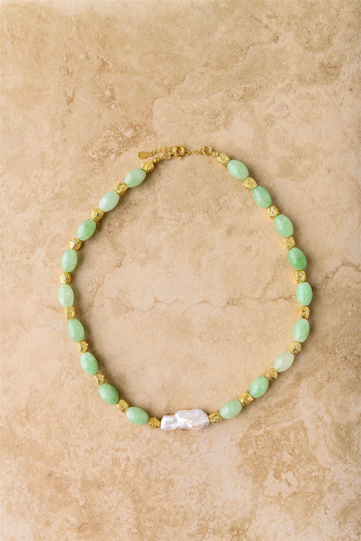 Necklace with green beads and a gold clasp on a beige background