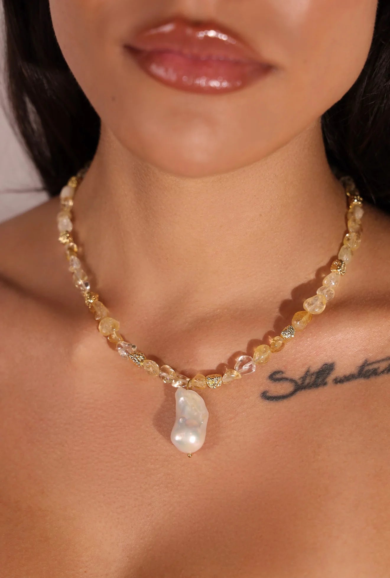 Necklace with a large pearl pendant worn by a person with a tattoo on their chest.