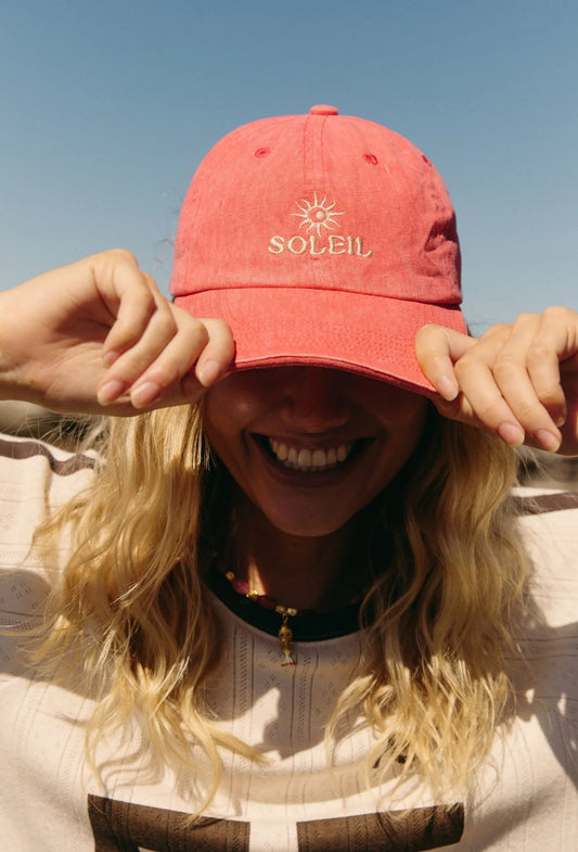 Person wearing a red cap with 'Soleil' logo against a clear blue sky