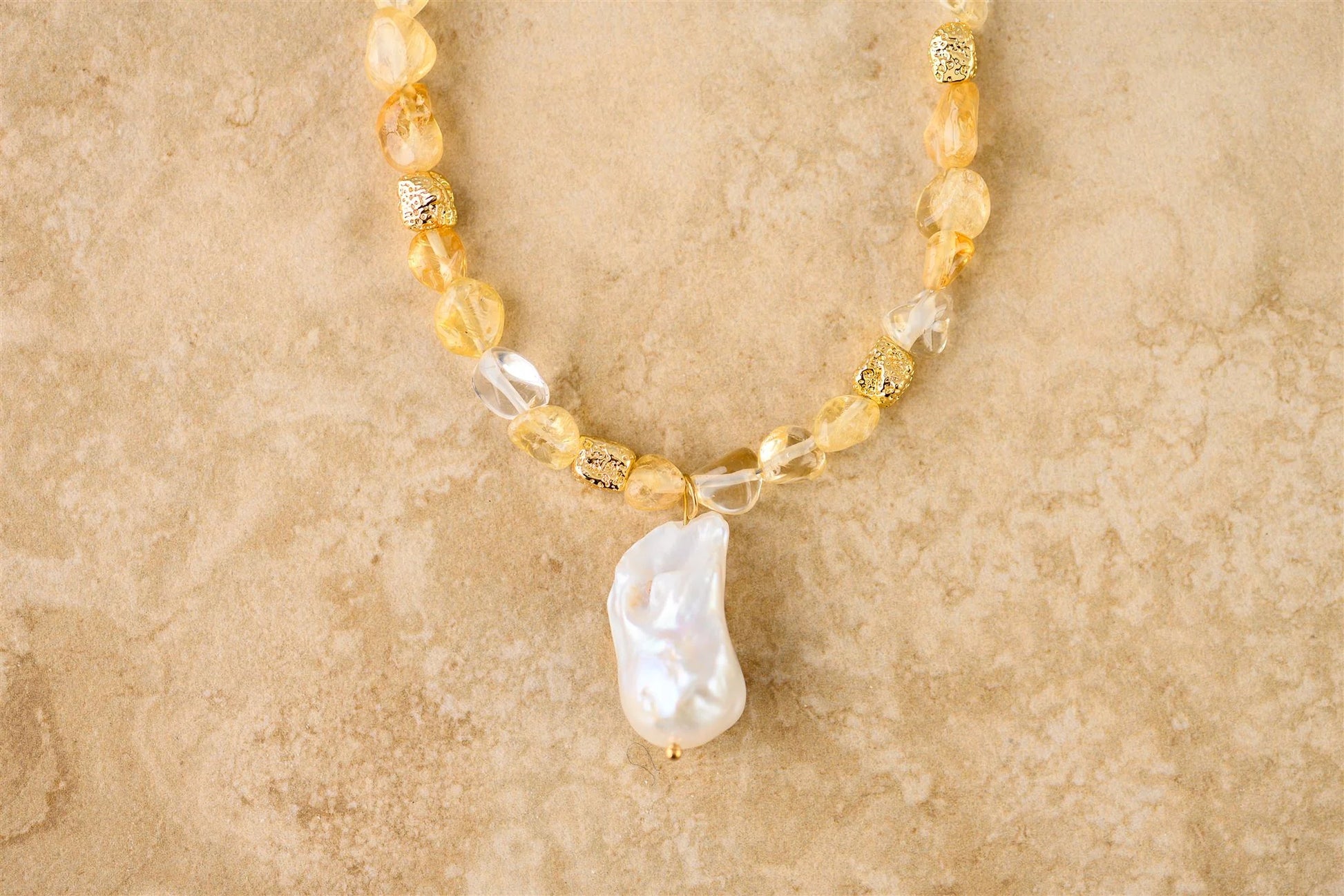 Necklace with yellow beads and a large pearl pendant on a beige background
